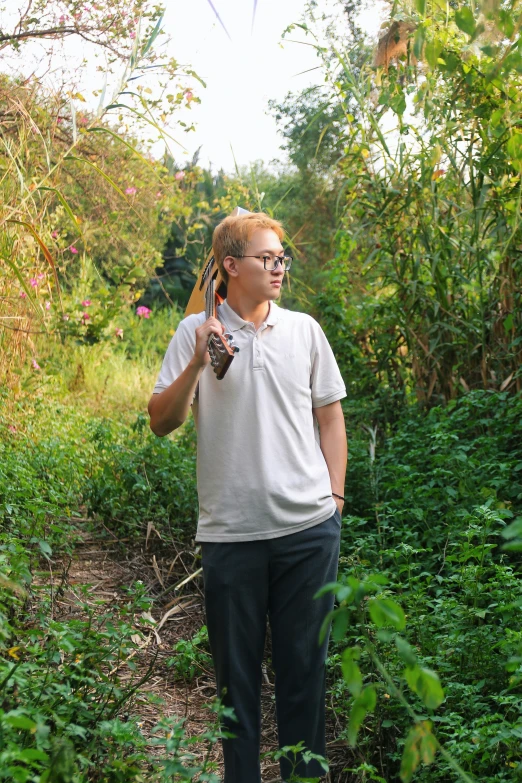 a young man with glasses stands near green plants