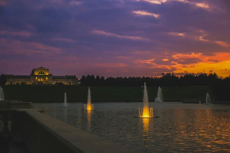 fountains in a pond at dusk with a building on the far side