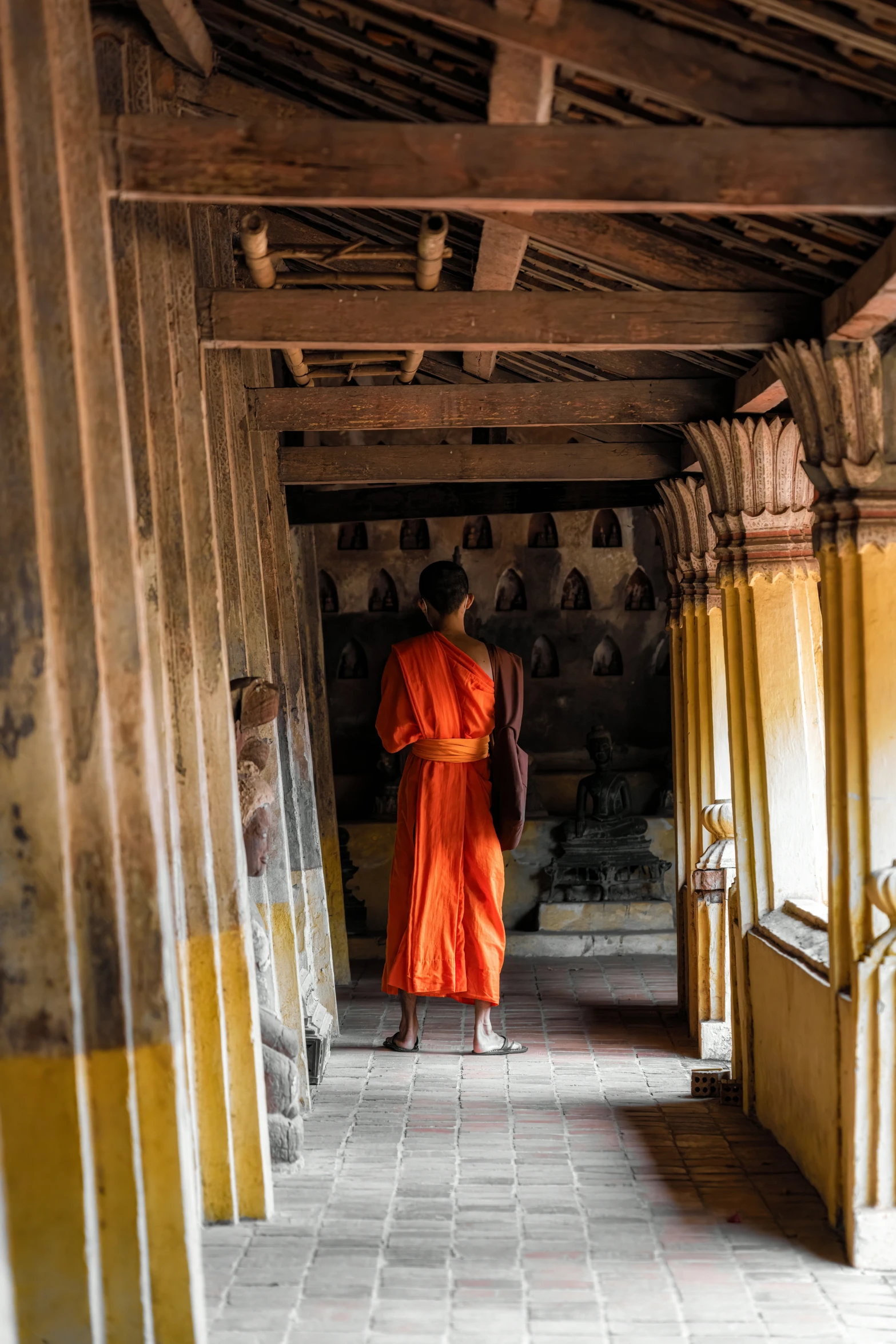 man in orange robes walking through large columns
