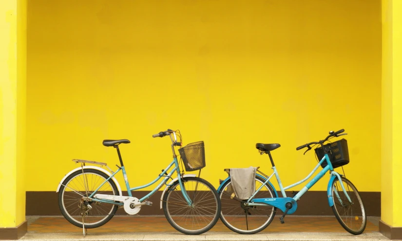 three bicycles are standing against a yellow wall