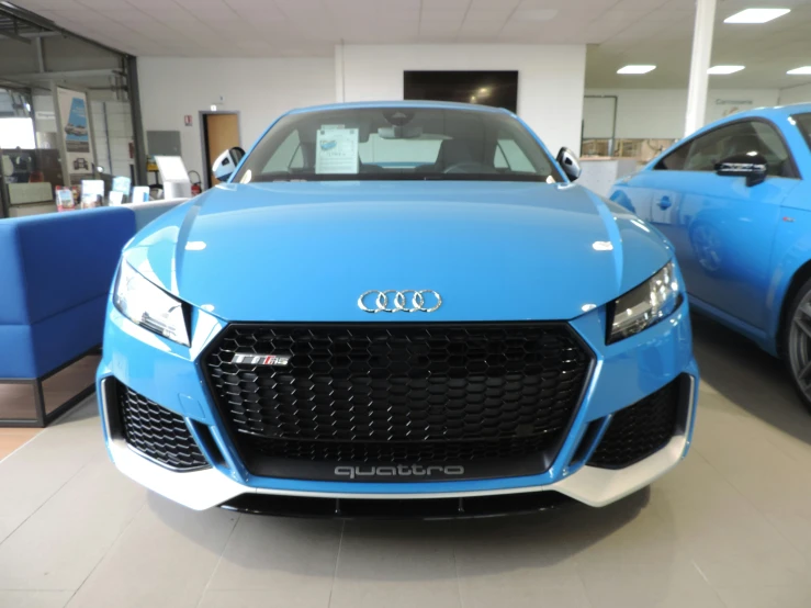 two blue sports cars in the middle of a dealers showroom