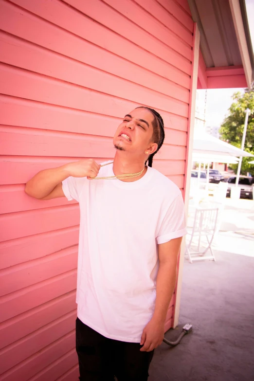 a man wearing a shirt and a necklace in front of a pink wall