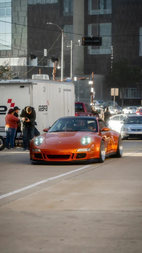 an orange sports car stopped in traffic at a stop light