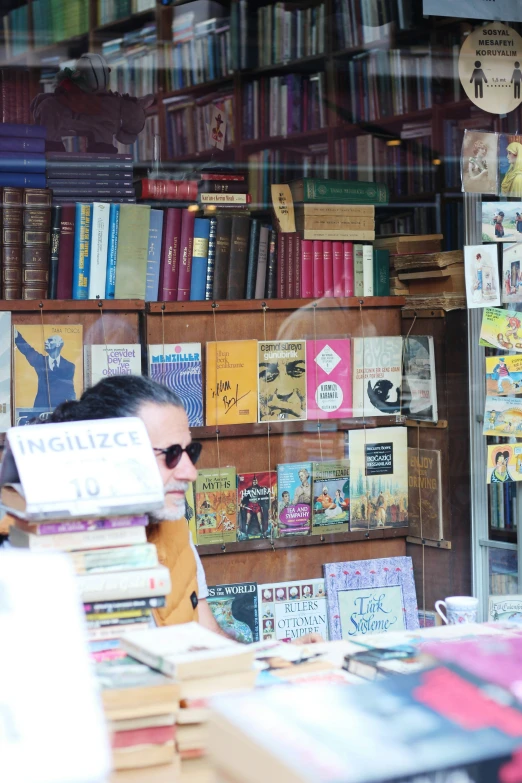 man reading in a book shop with a large amount of books on the shelves behind him