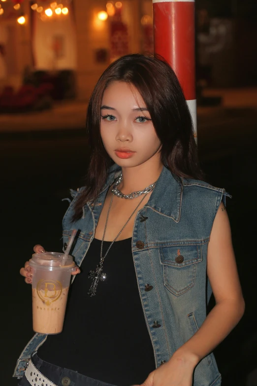 a girl is holding up a drink on a street