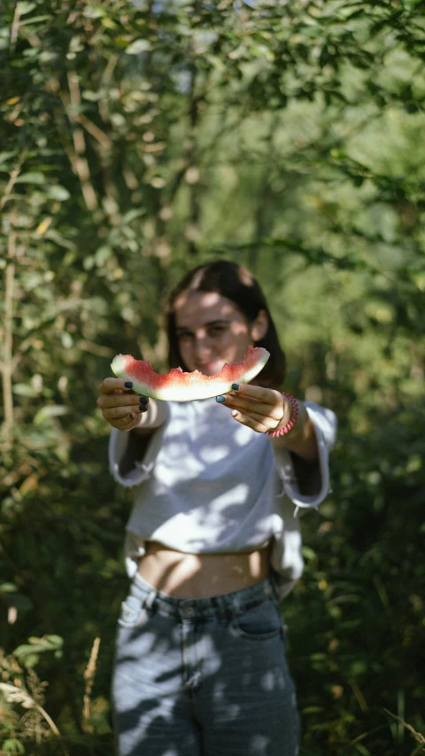 a woman holding up a piece of watermelon in the woods