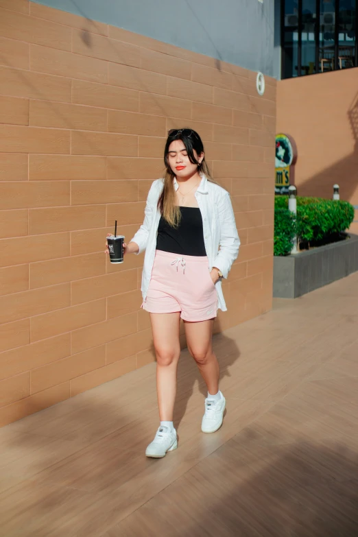 woman in pink shorts and a white jacket holding a drink