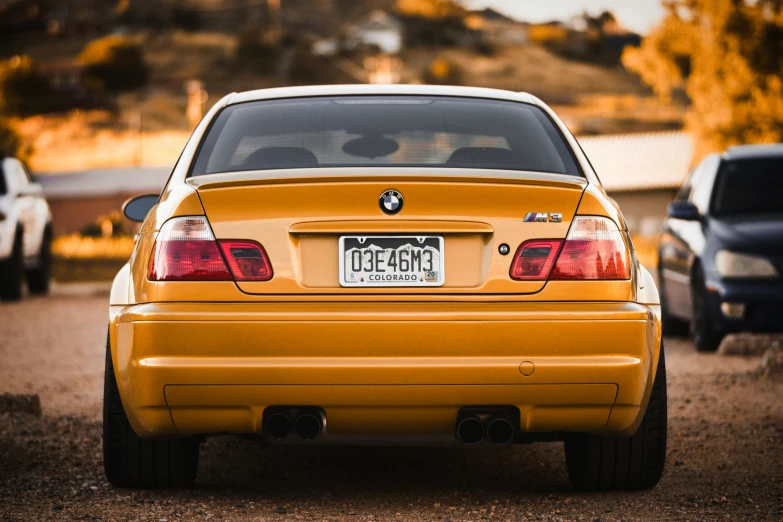 the rear end of a yellow car parked on dirt