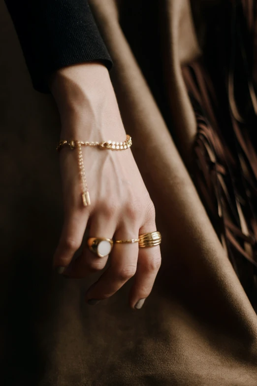 a hand with a gold chain, beads and a pearl celet