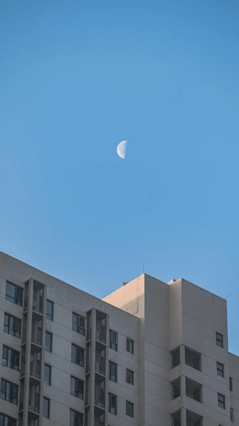 the moon in a blue sky next to an apartment building