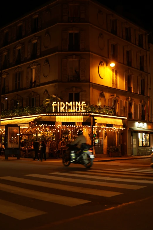 a moped rides past a building with a lit up sign at night