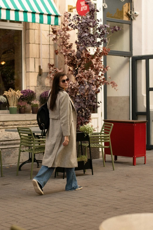 woman in beige coat walking down the street with a backpack