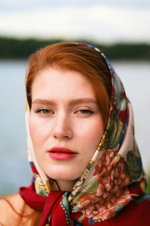 red - headed woman wearing scarf with hood and water in background