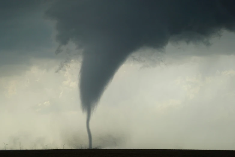 a large tornado shaped cloud towering over a dry field