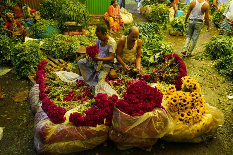 three people looking at a flower market while another man puts the flowers in bags