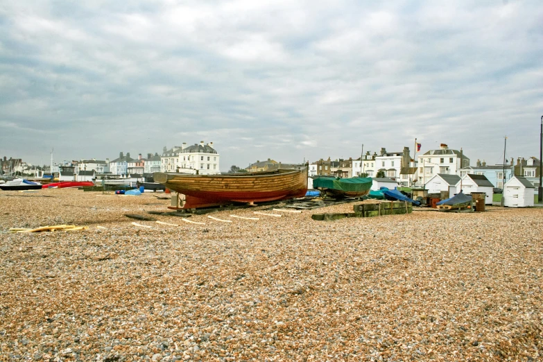 several boats sitting on a shingled beach in front of a row of houses