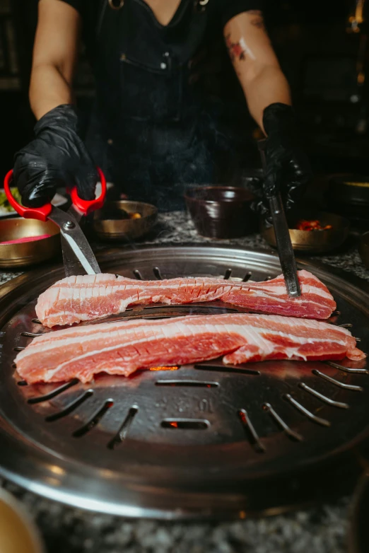 two pieces of meat being cut on a grill with a pair of gloves