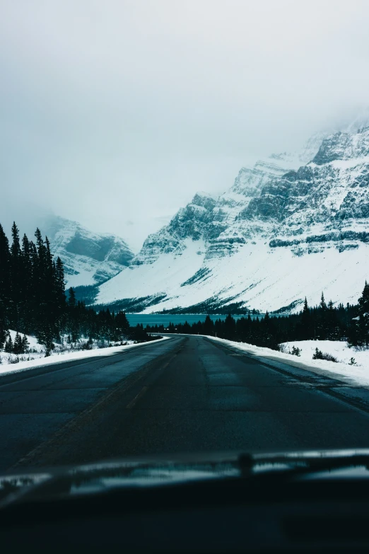 snowy mountains stand above an empty highway with trees and bushes