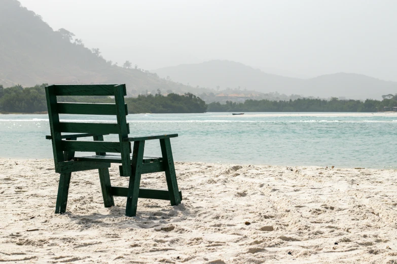 a bench with a chair on the beach near water