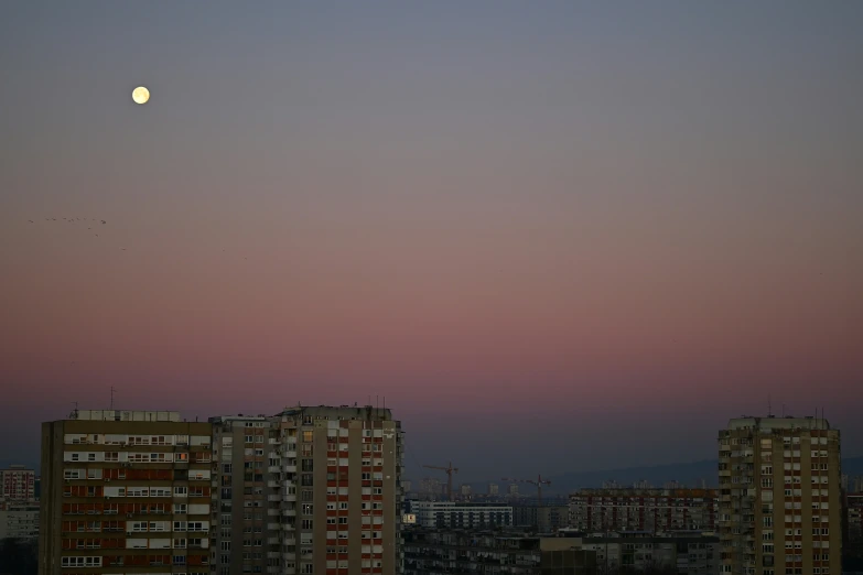 a full moon is setting over some tall buildings