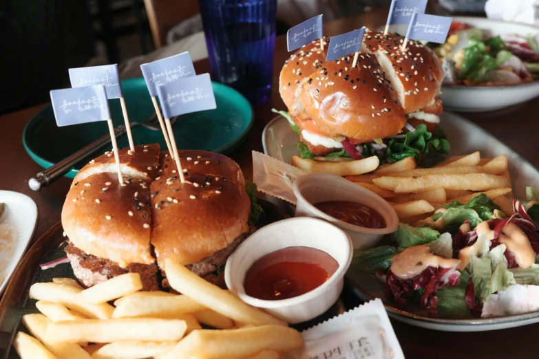 two hamburgers and fries on plates with tiny flag toppers