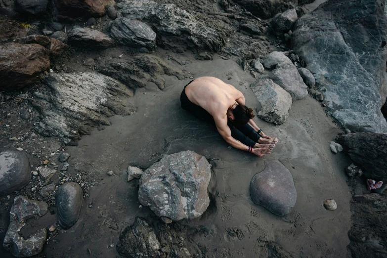 a man lying on a sandy beach near rocks