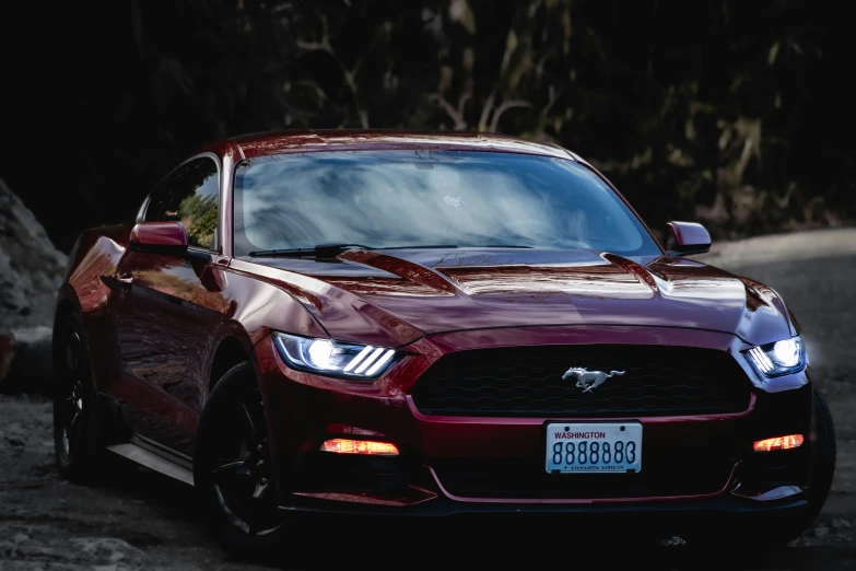 the red mustang parked in the dark near trees