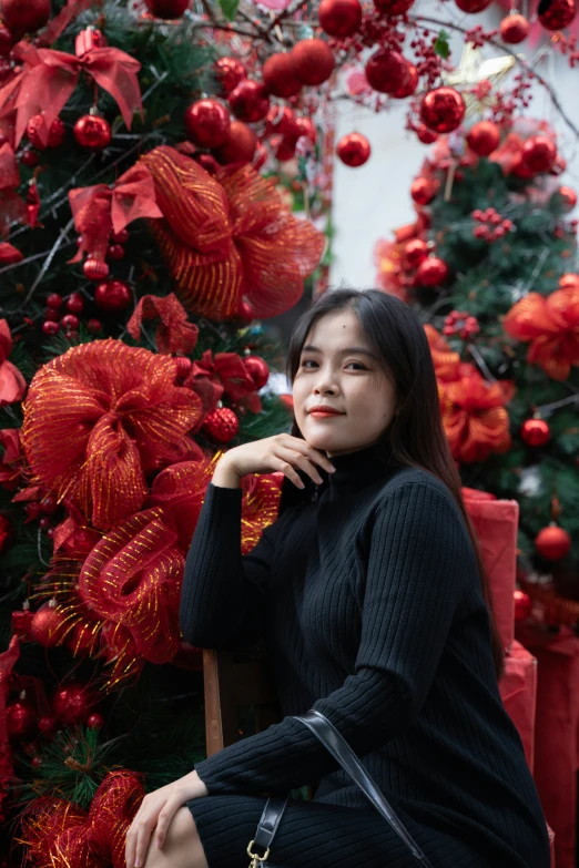 a woman in black sitting next to a christmas tree