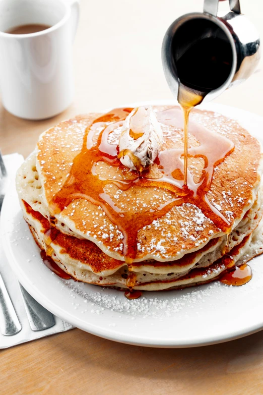 a person pouring syrup on top of pancakes