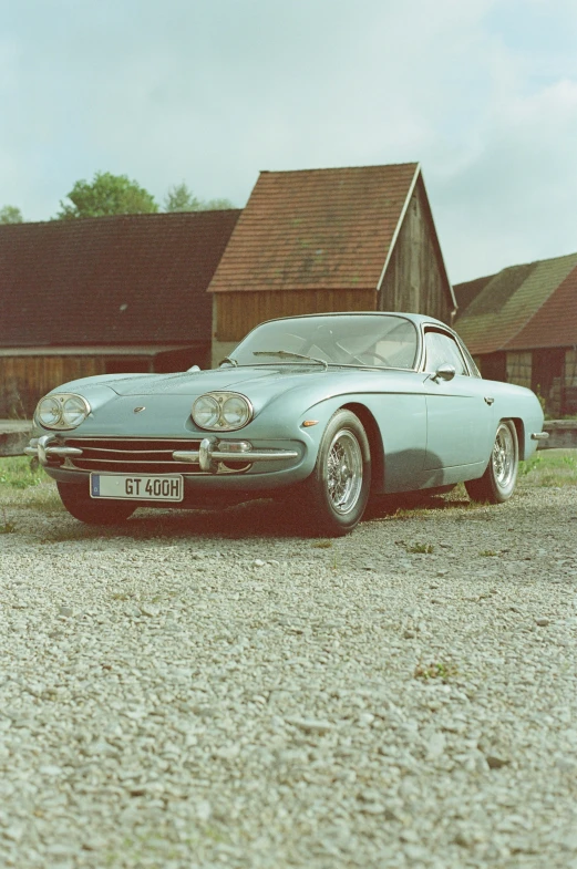 old car parked in front of a barn on gravel