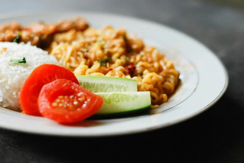 a white plate with rice, tomatoes and cucumber
