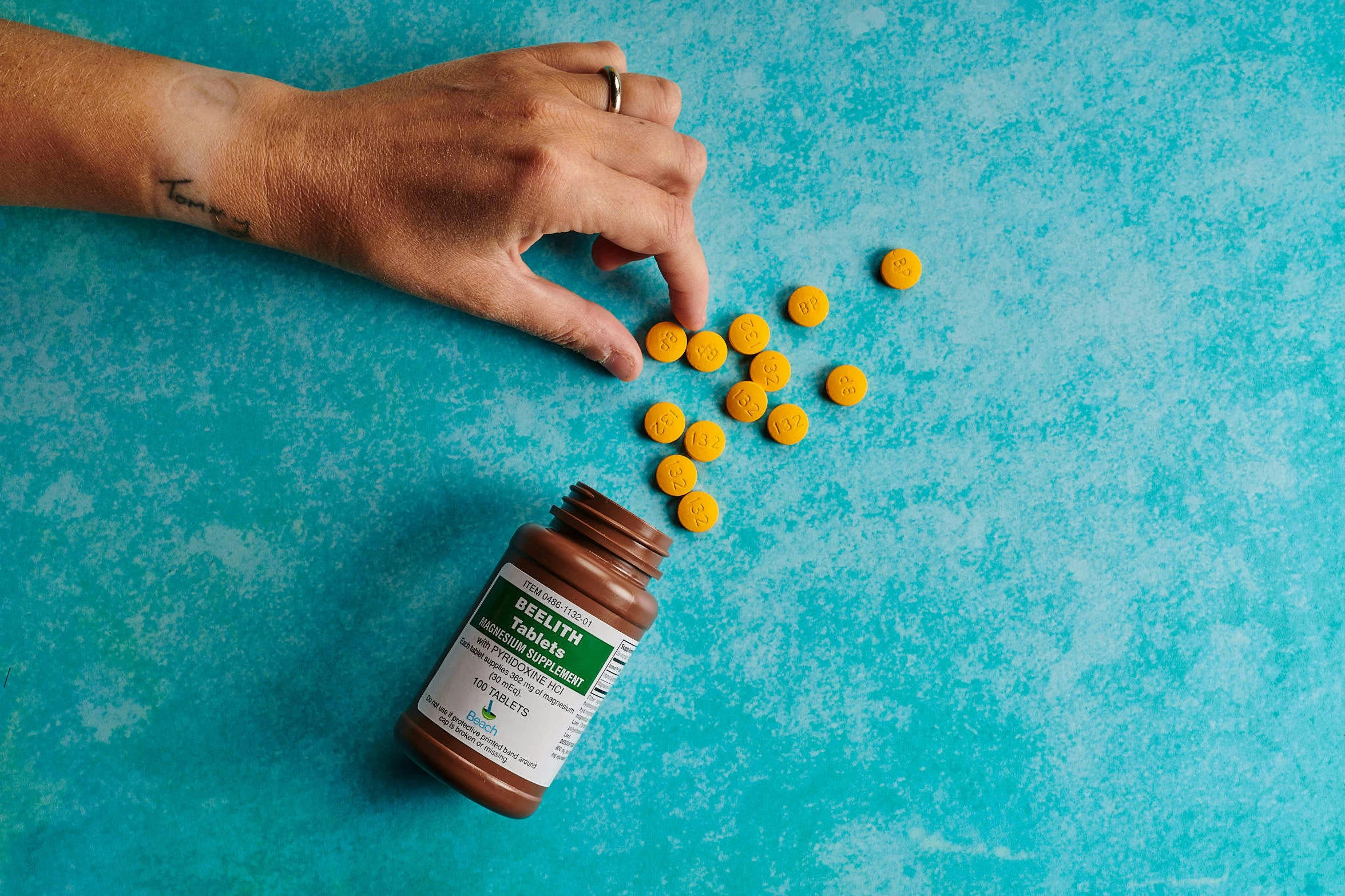 a hand reaching for pills with small yellow ones coming out