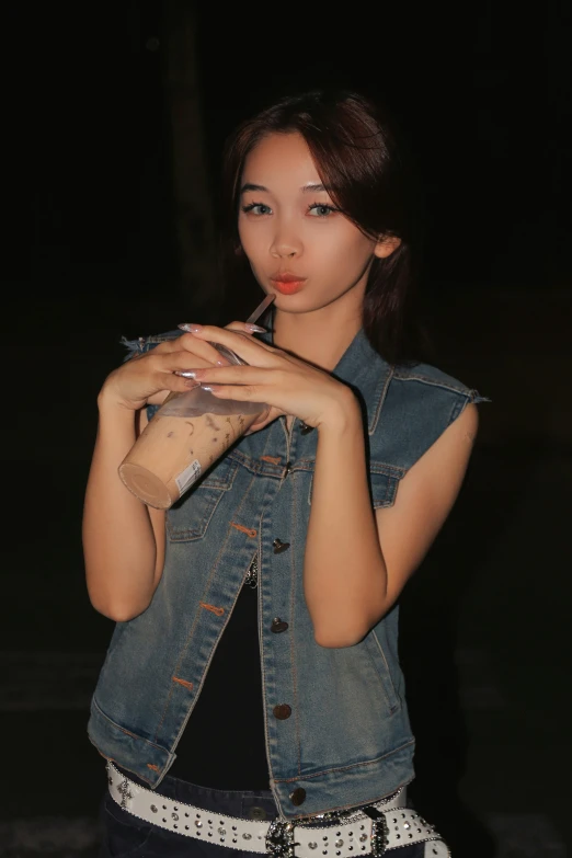 a young woman smokes an cigarette while wearing a jean vest