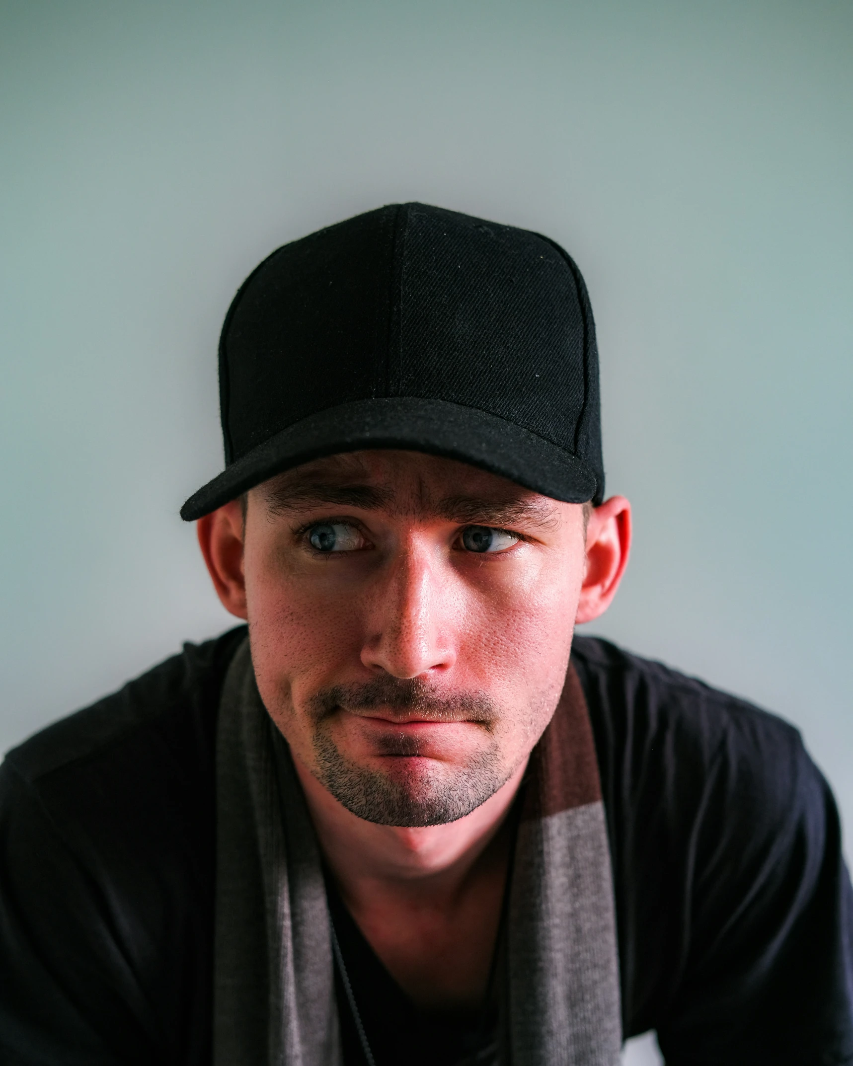 a man with a hat, scarf and cap in front of a wall