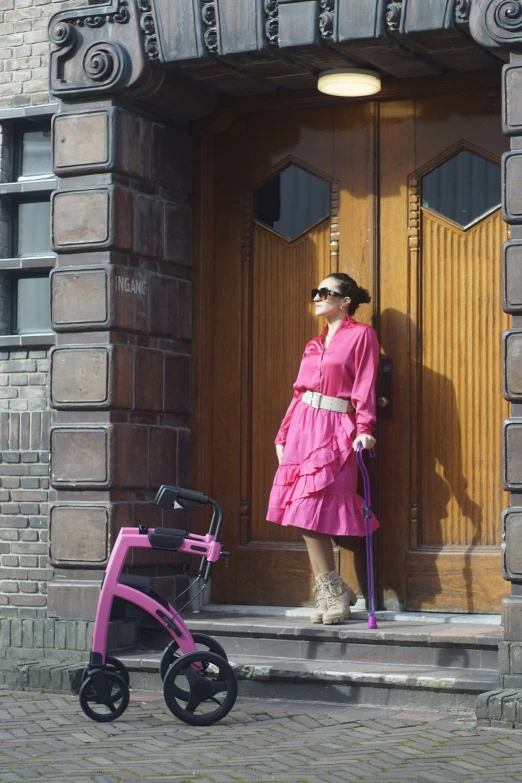 a woman in pink dress standing in front of wooden door with wheeled her