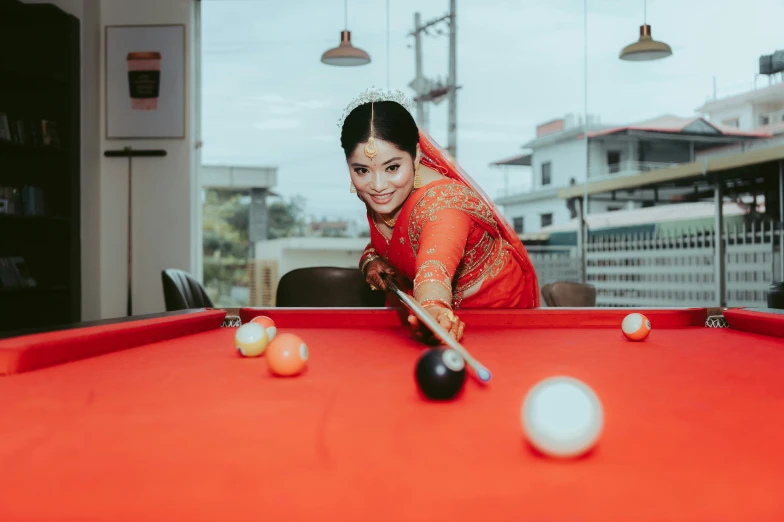 a woman in a red veil leans on a pool table