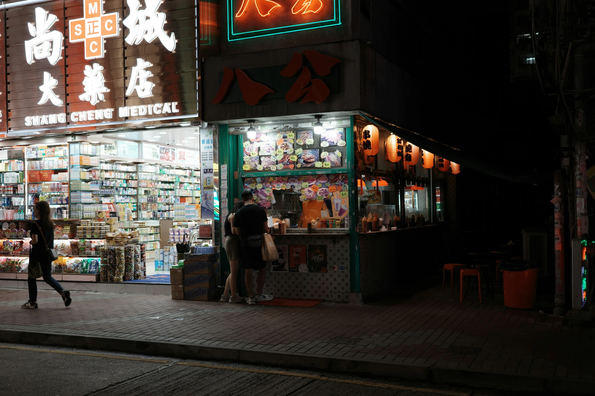 two people walk past a large building with lit signs