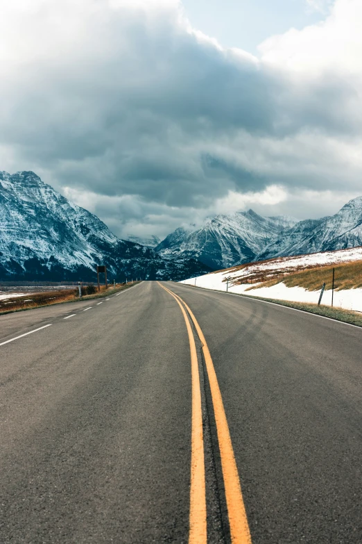 a rural road in the winter with snow capped mountains behind