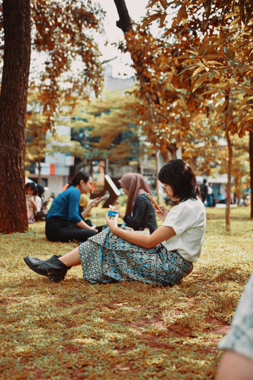 two women are sitting in a park on their cell phones