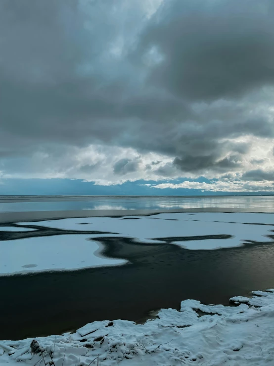 an ice - covered lake under dark skies and some clouds