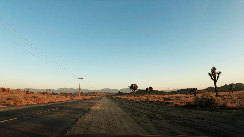 an empty road in the desert with telephone poles