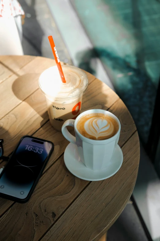 a cappuccino coffee is on the table near an open smart phone