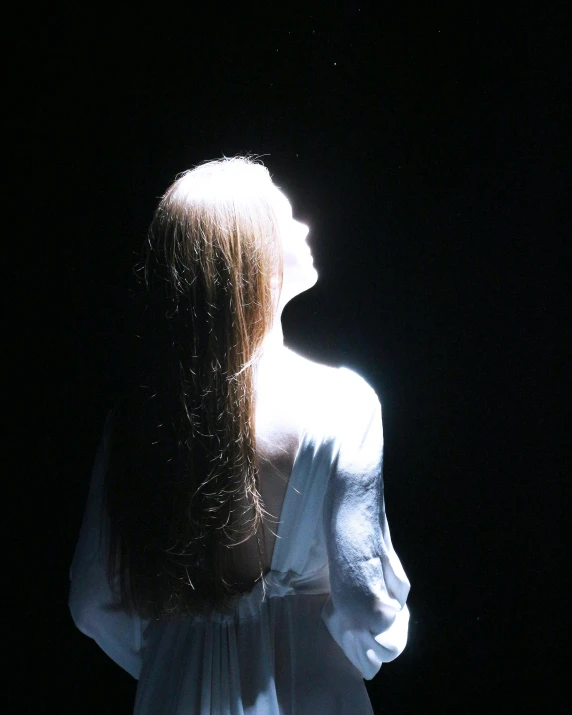 a woman standing in the shadows in front of a dark background