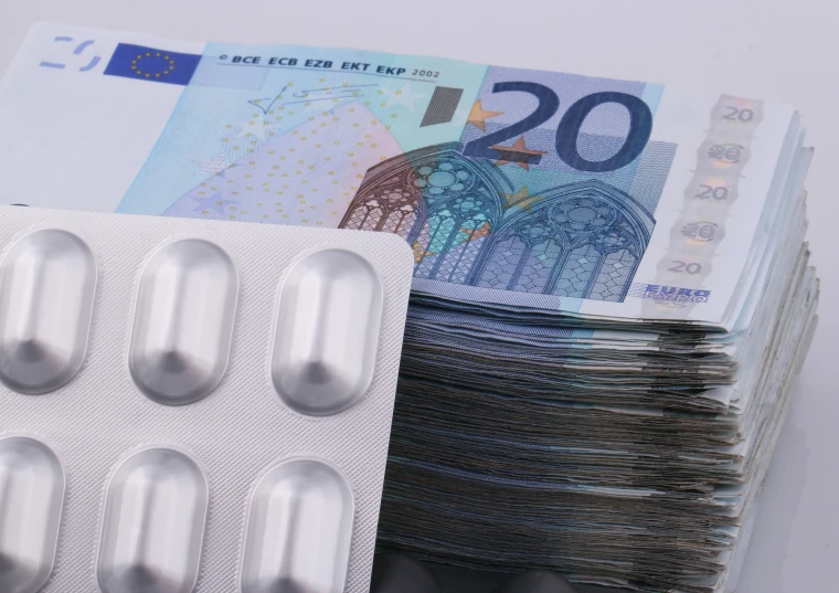 some pills in front of a stack of twenty euro bills