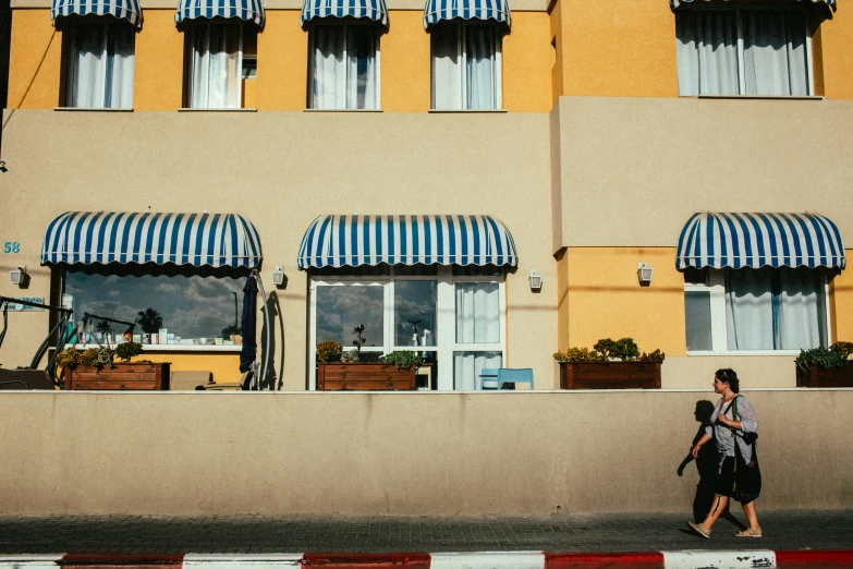 woman in a backpack is walking past a yellow building