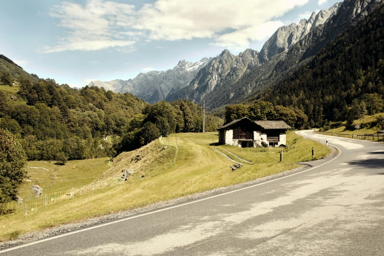 an empty street in the mountains with a house and mountains in the background