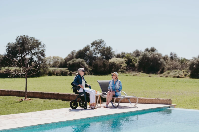 two older women in a wheel chair sitting on a small bench near a pool