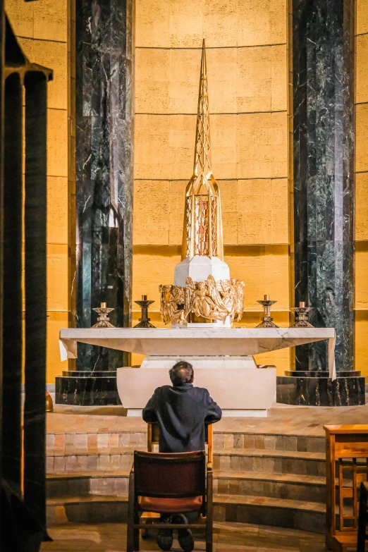 a priest is sitting and praying in front of a tall golden alter