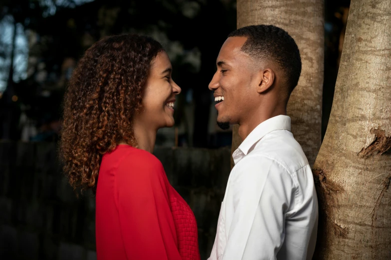 a couple smiles and laughs next to some trees