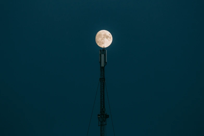 a white moon seen above an antenna in the night sky